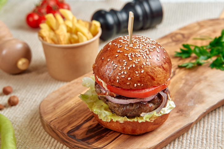 Delicious Gourmet Burger with Fresh Toppings, Served on a Wooden Board with Crispy Fries and a Side of Vegetables for a Perfect Meal Experience