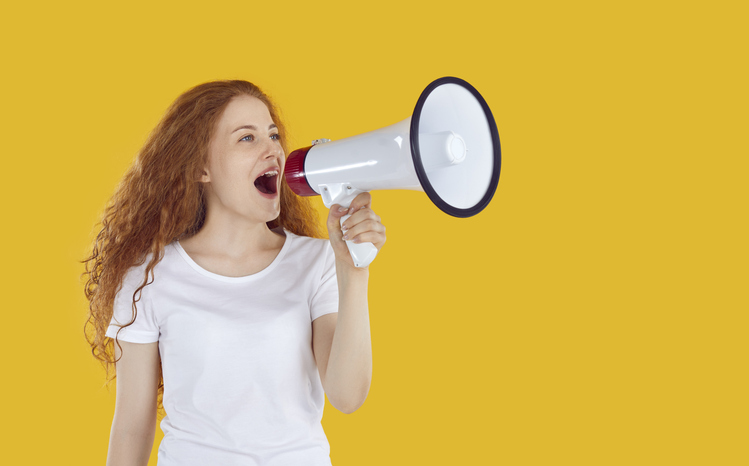 Expressive girl using megaphone to announce discounts and sales isolated on yellow background.